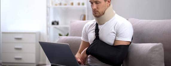 man with arm in sling looking at laptop computer